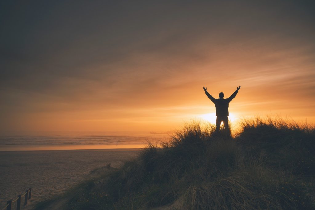 homme libéré de ses blocages lève les bras face au coucher de soleil
